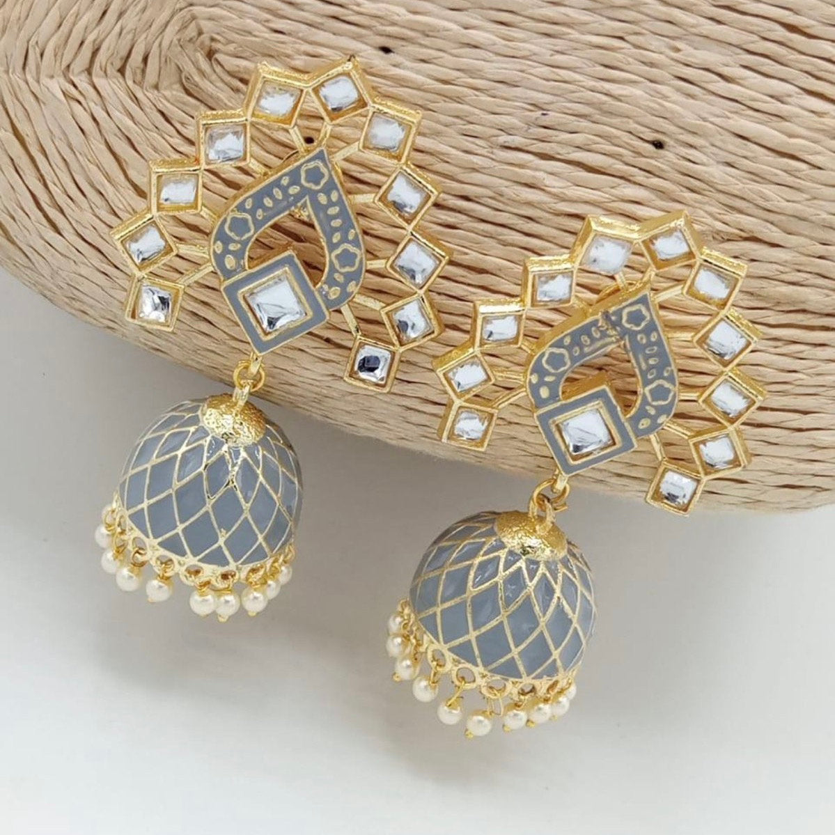 Decorative earrings with gold and gray design on a textured beige surface